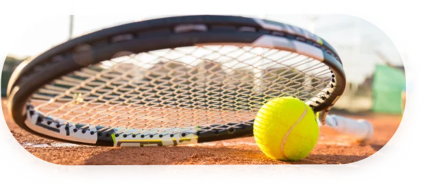 Gros plan sur une raquette de tennis et une balle sur un court en terre battue, baigné de soleil, avec un joueur flou en arrière-plan. L'ambiance est dynamique et concentrée.